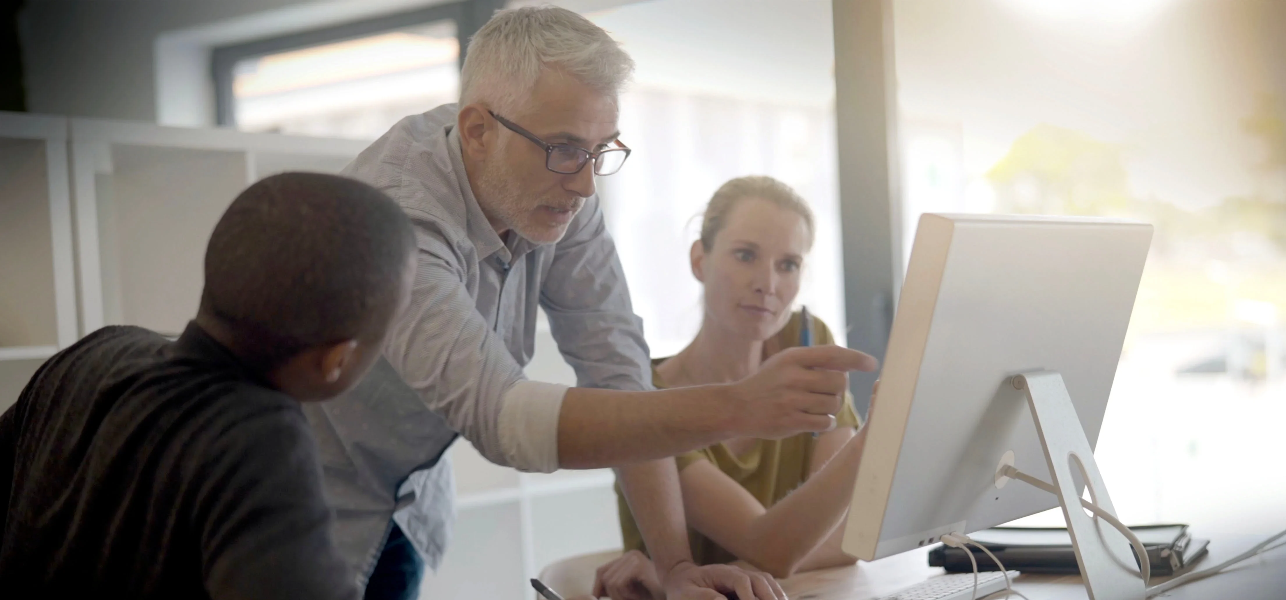 Man training two younger employees on a computer