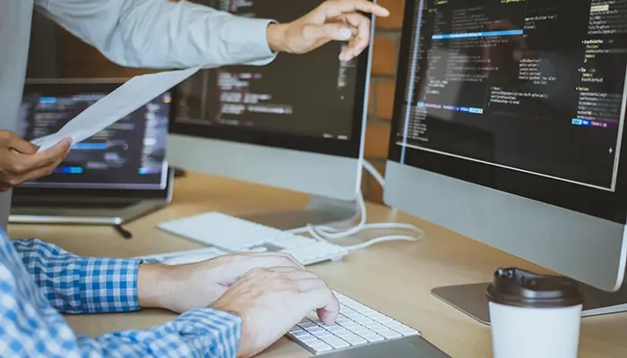 Two people working on web code on a desktop computer.