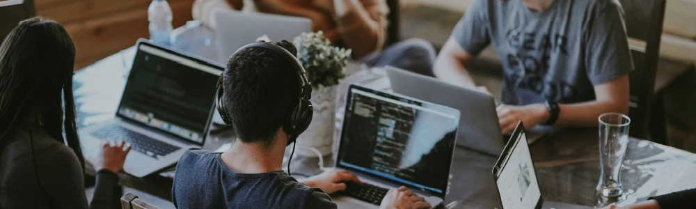 Man working at a computer in office setting with co-workers