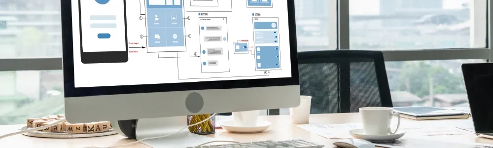 Image of a desktop computer with wireframes and user flow schematics.
