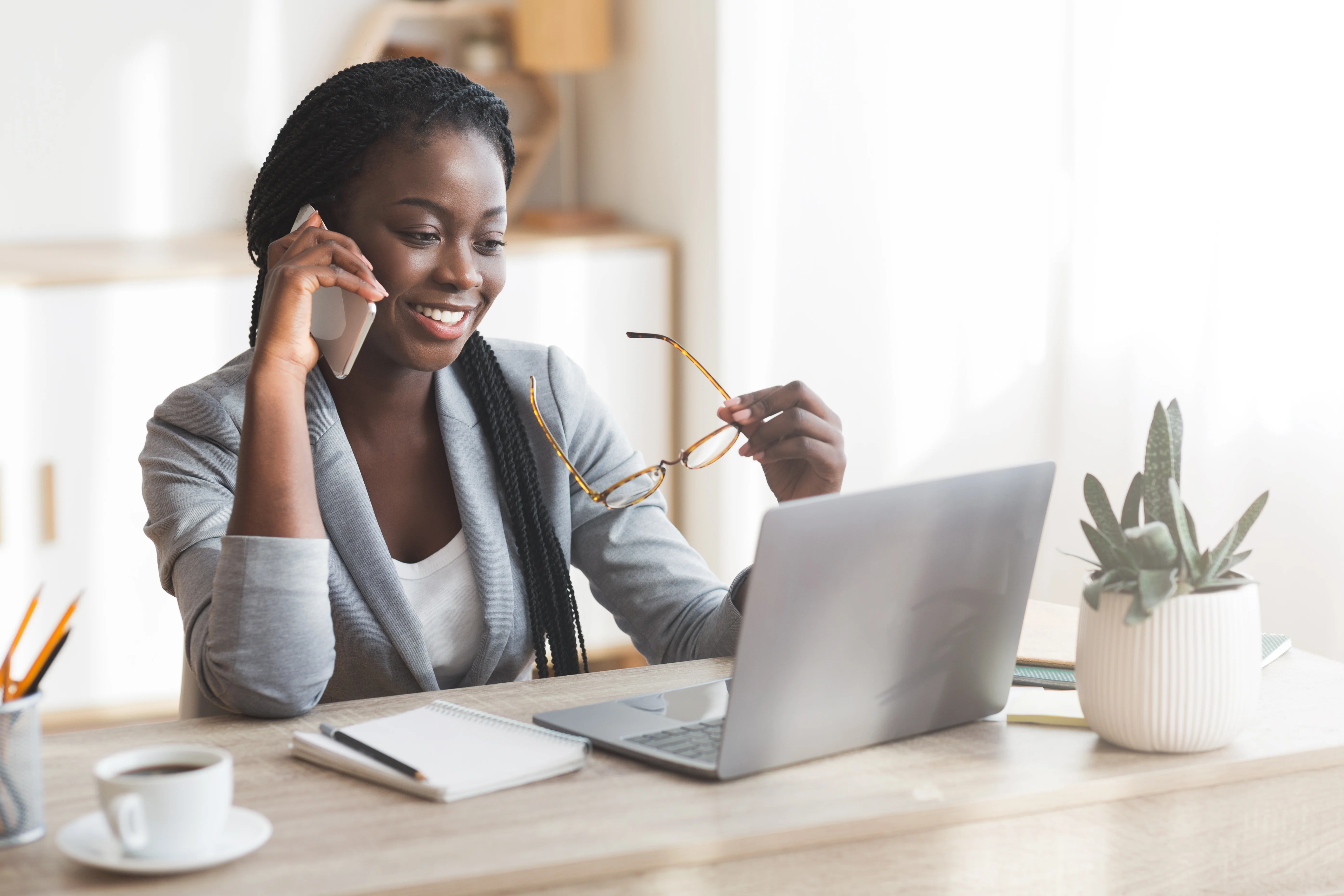 Woman holding eye glasses talking on phone in front of laptop
